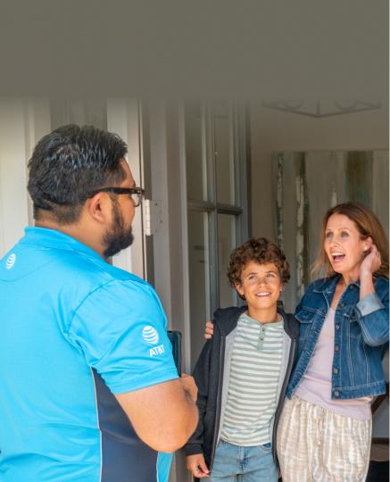 Mother and son stand at front door laughing and chatting with friendly AT&T installation technician.