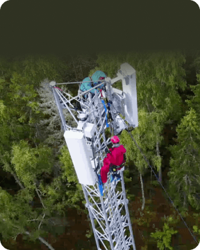 Engineers work high up on Cellular Transmission Tower with forest below.